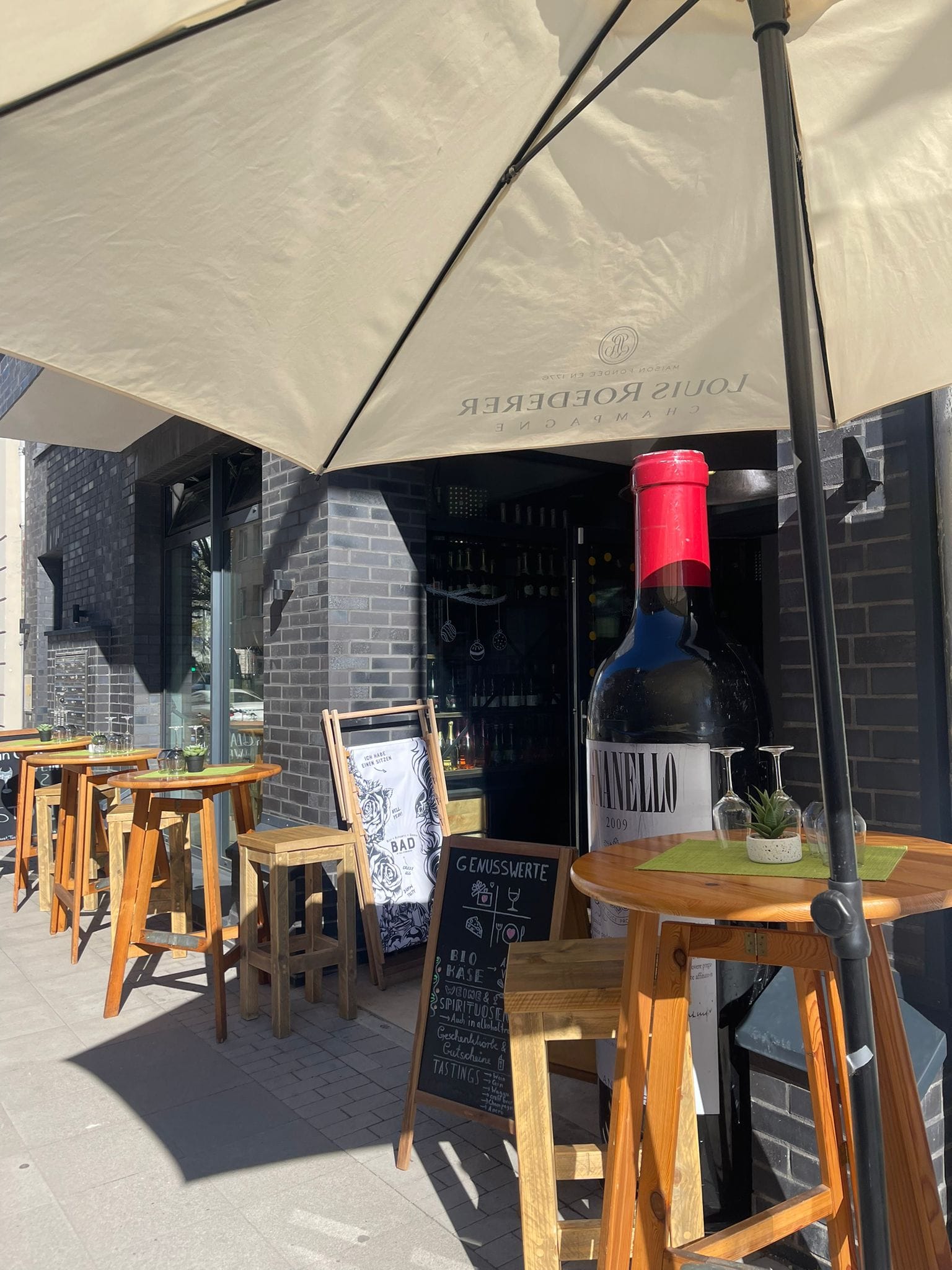 Außenterrasse der Weinbar mit Stehtischen und großer Magnumflasche