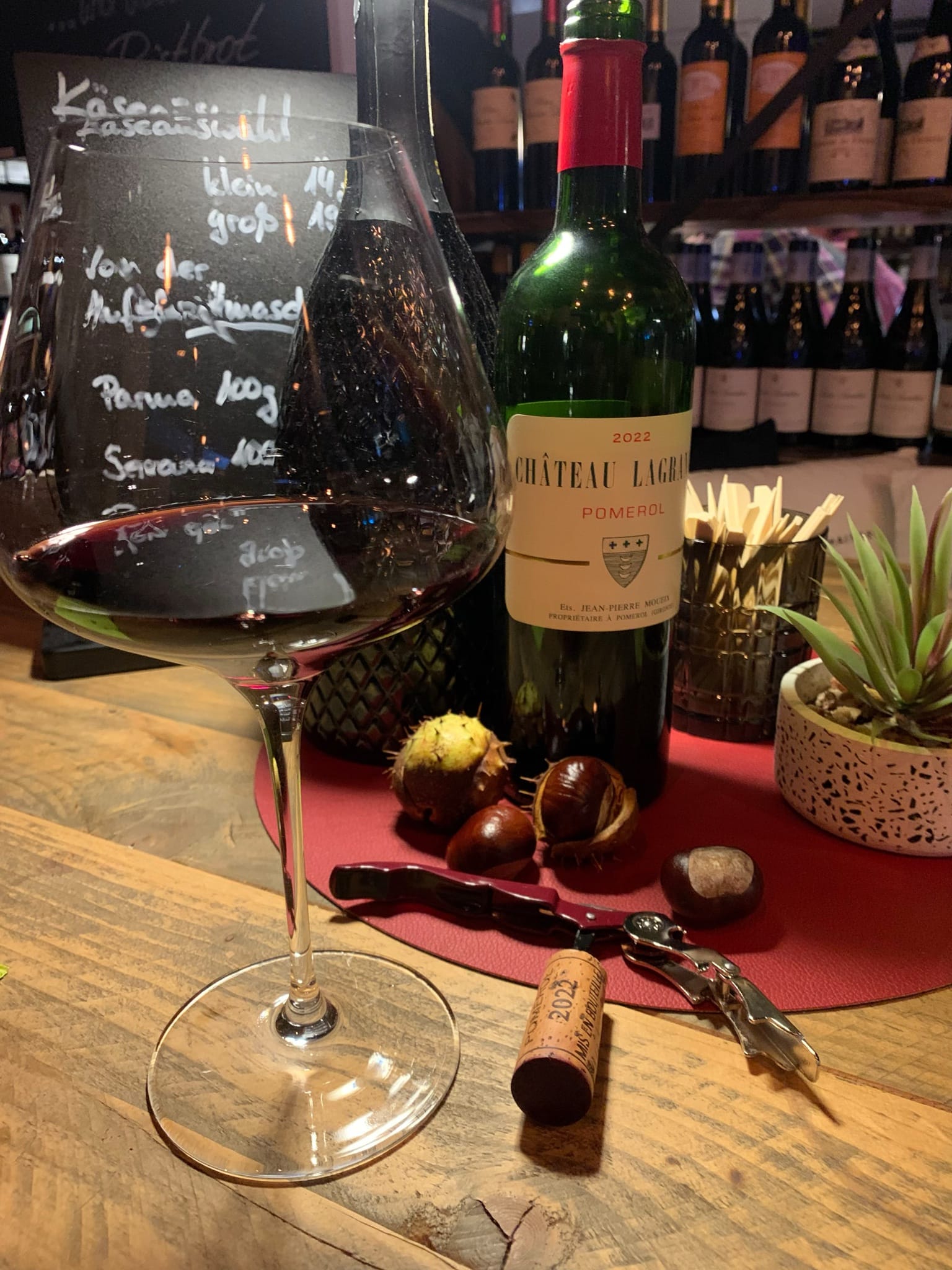 Glas Rotwein und eine Flasche Château Lagrange Pomerol 2022 mit Kastanien am Tresen der Weinbar
