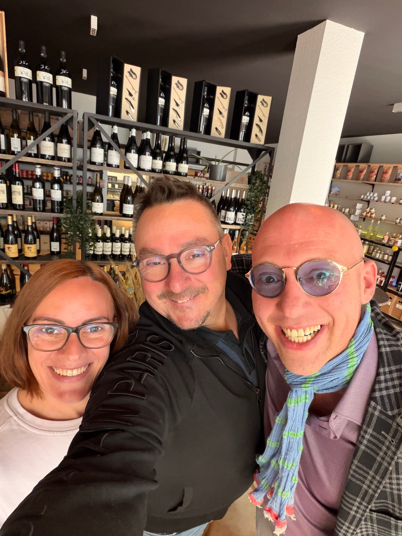 Carina, Sascha und Philipp vor dem Weinregal der Weinbar